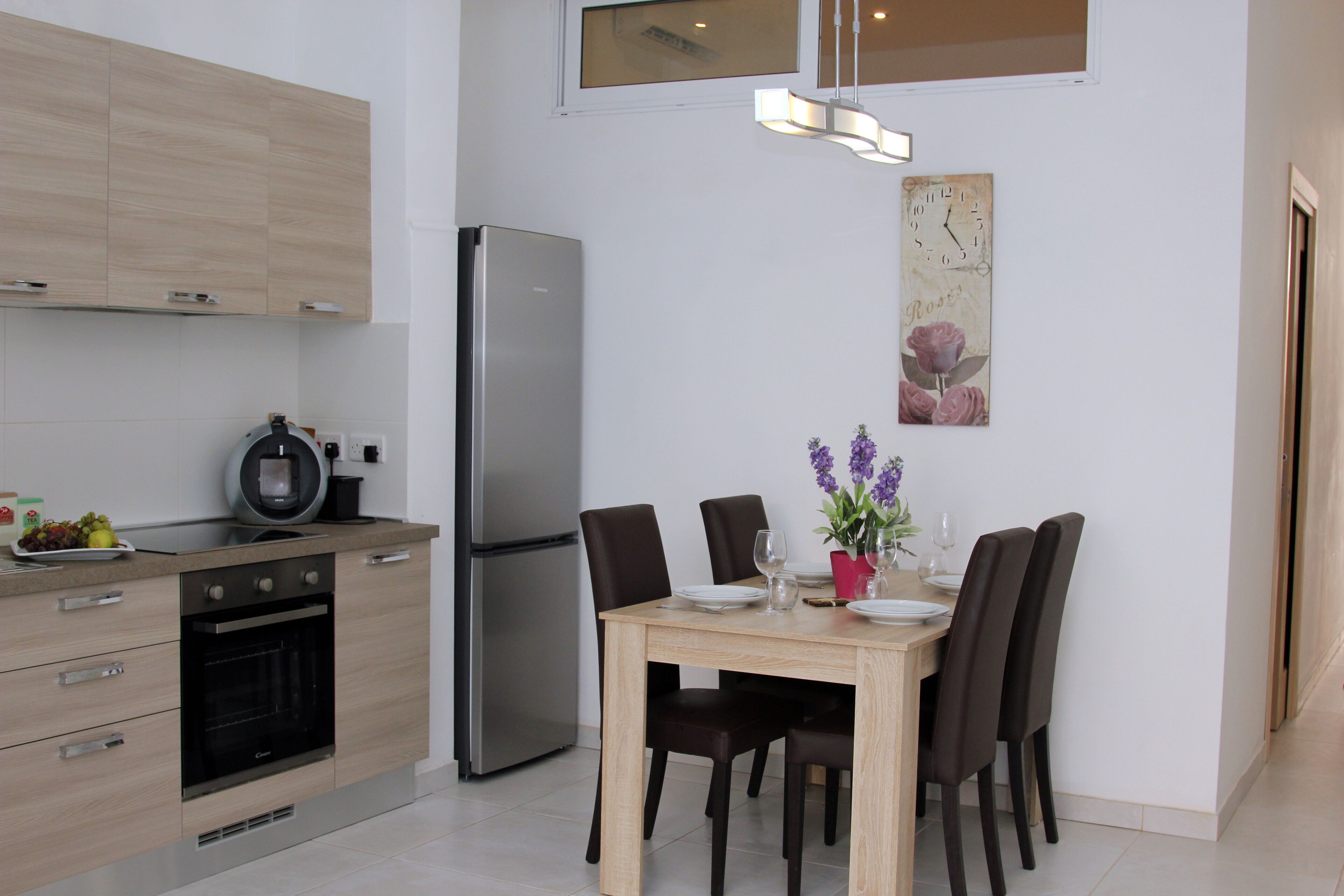 A modern kitchen with a built-in oven, a refrigerator, and a dining area with a wooden table and chairs.