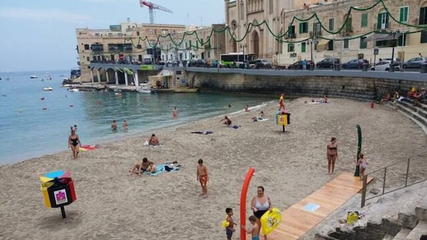 A beach with people sunbathing and swimming, a lifeguard tower, and buildings in the background. - Entire home. Private entrance. 5 minutes walk to shops and sea front.  (Sliema)