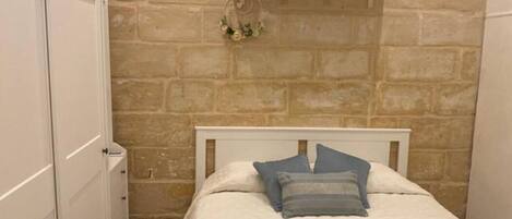 Une petite pièce chaleureuse, avec un lit, une armoire blanche et un mur en pierre.