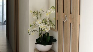 A hallway with a wooden console table, a white vase with orchids, and a mirror with wooden panels and metal hooks. - Entire home. Private entrance. 5 minutes walk to shops and sea front.  (Sliema)