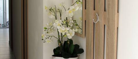 A hallway with a wooden console table, a white vase with orchids, and a mirror with wooden panels and metal hooks.