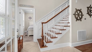 A staircase with white railings and wooden steps, leading to a room with a bed and a sign reading "Beach House".