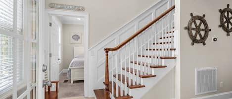 Una escalera con barandillas blancas y peldaños de madera que conduce a una habitación con una cama y un letrero que dice "Beach House".