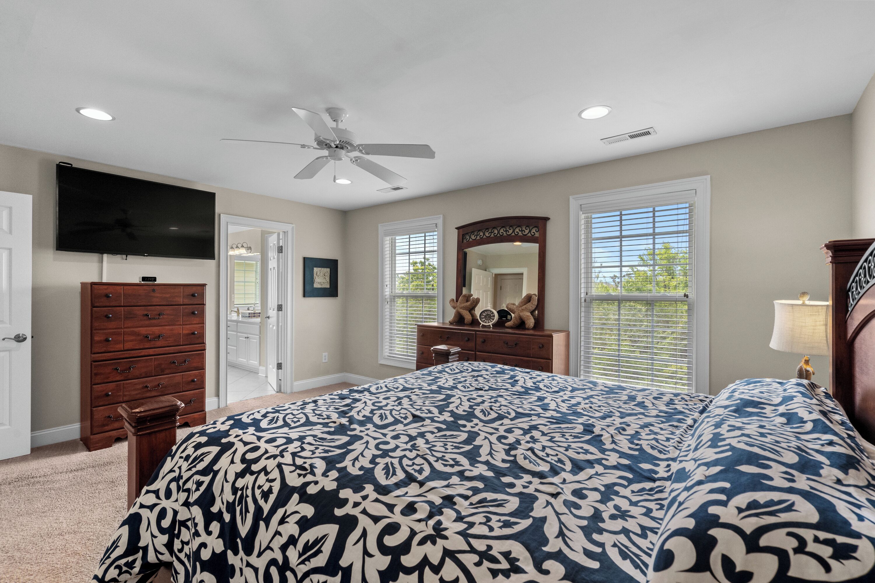 A bedroom with a large bed, a ceiling fan, a TV, and a dresser.