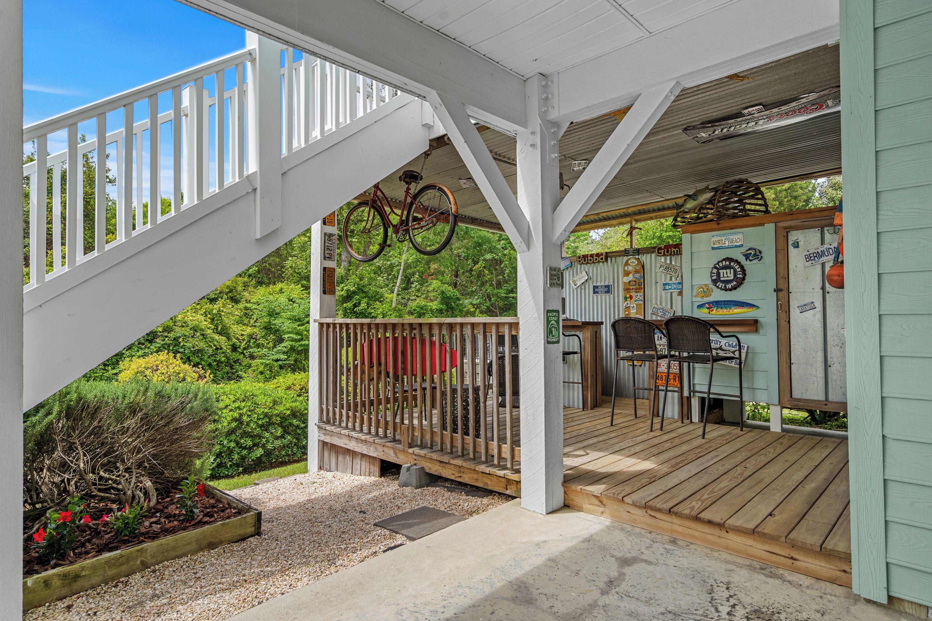 A covered outdoor area with a wooden deck, a bicycle hanging from the ceiling, and a small bar area with chairs and tables.