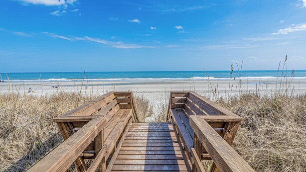 A wooden boardwalk leading to a beach with a clear blue sky.