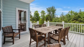 A wooden deck with a table and chairs, a white railing, and a view of trees and sky.