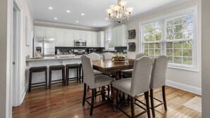 A modern kitchen with white cabinets, a wooden dining table with six chairs, and a chandelier.