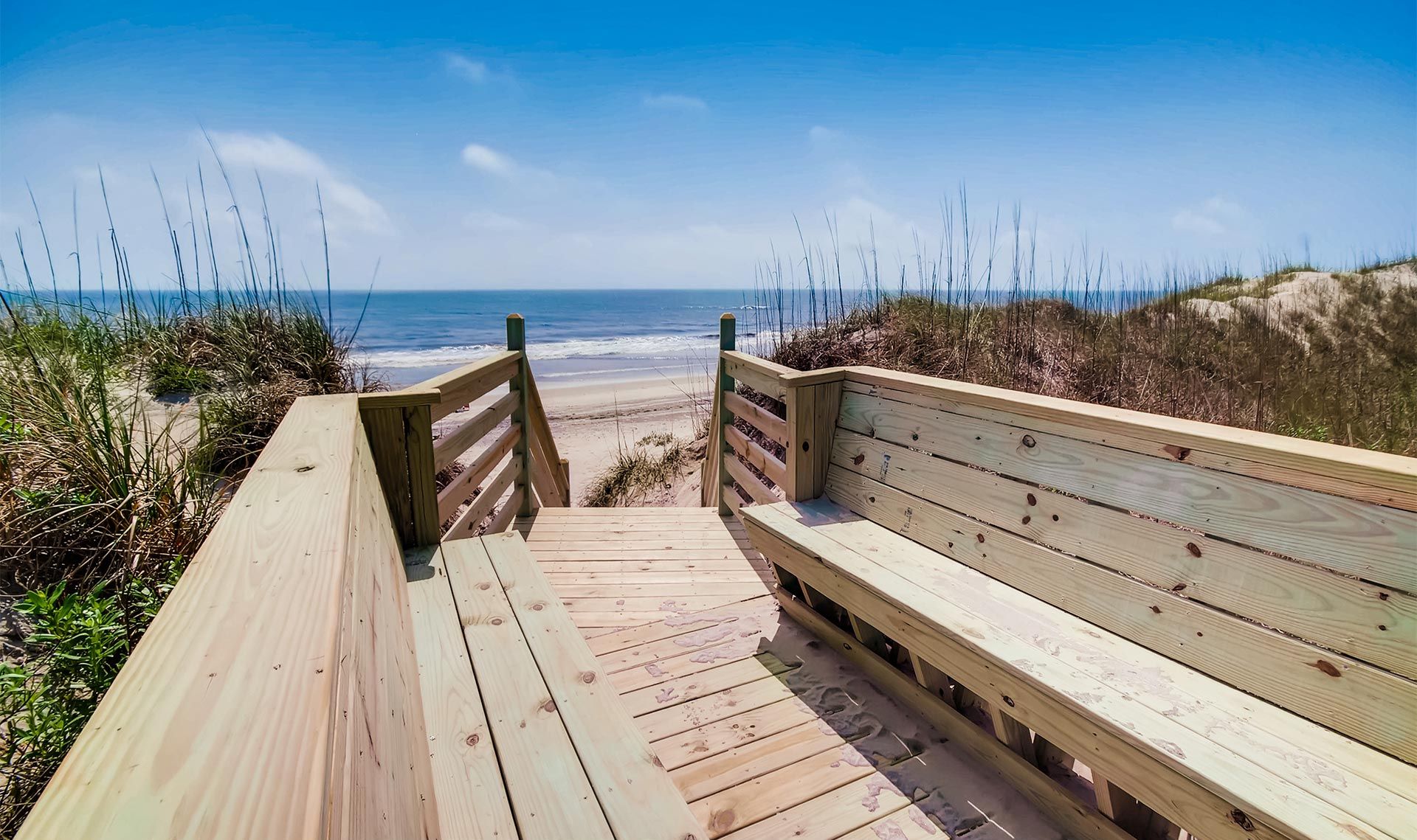 Une promenade en bois menant à une plage où se trouve un banc.