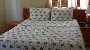 Een bed met een palmboom dessin, een houten hoofdbord en passende kussens.