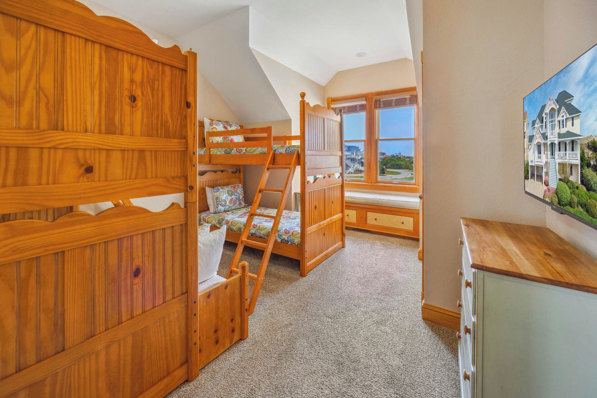 Une chambre avec un lit superposé, un coin lecture près de la fenêtre et un tableau représentant une maison.