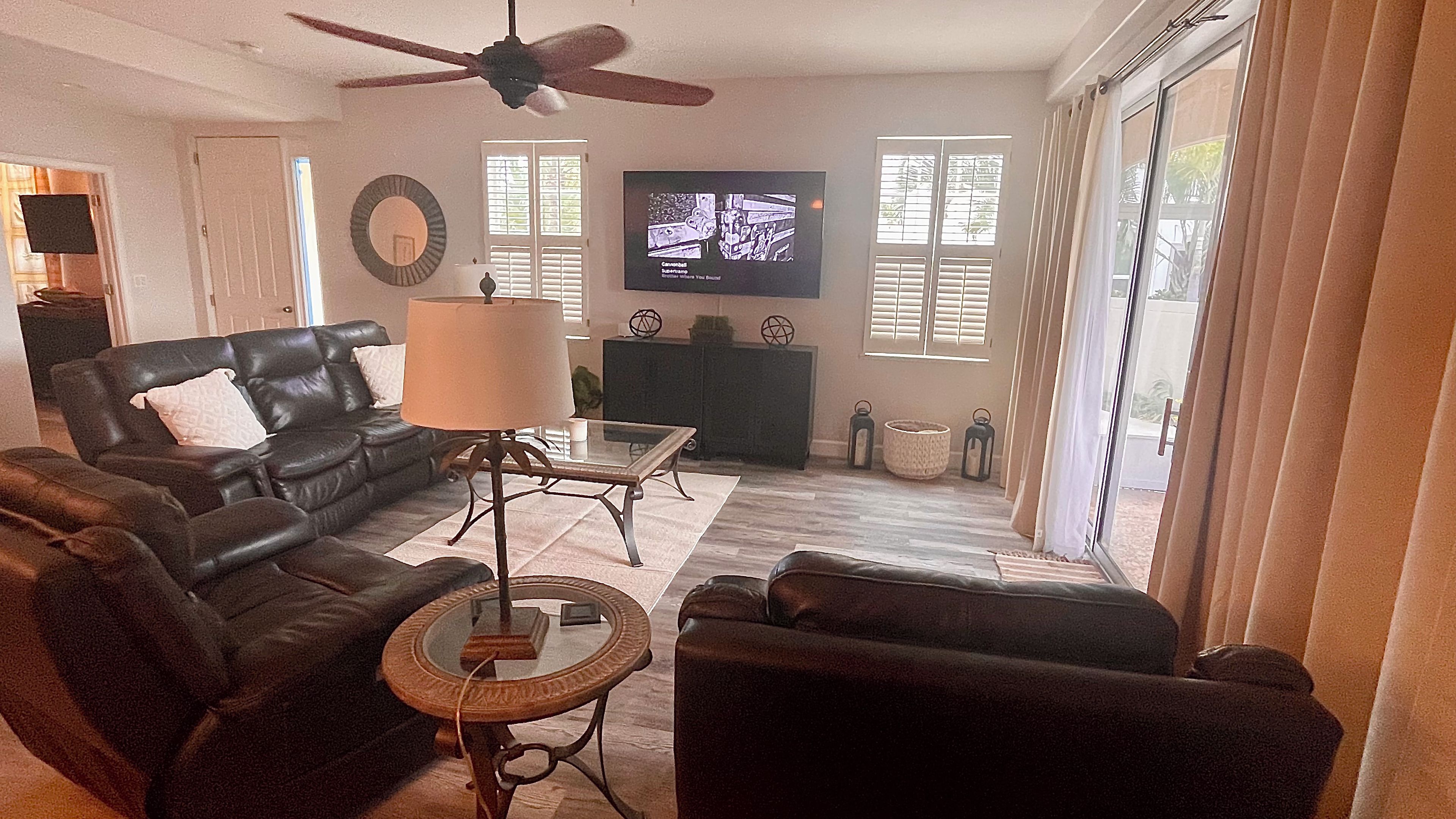 Un salon avec un canapé en cuir, une table basse, un téléviseur et un ventilateur de plafond.