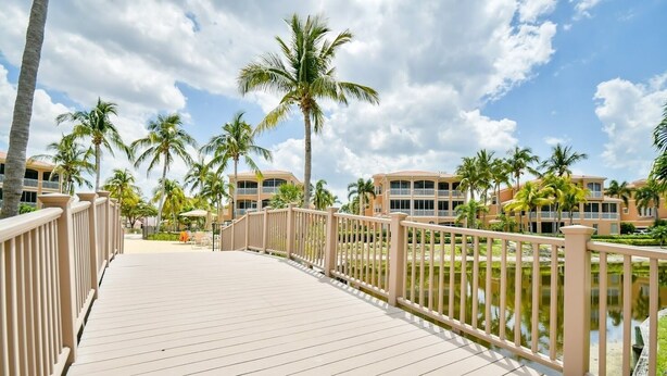 A wooden deck with a railing, palm trees, and a body of water in the background. - 3 Bedroom 2 Bath 2 Car Garage includes Golf Cart Usage (Punta Gorda)
