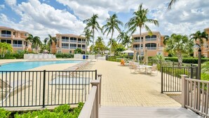 A resort pool area with a clear sky, palm trees, and a fenced deck with lounge chairs. - 3 Bedroom 2 Bath 2 Car Garage includes Golf Cart Usage (Punta Gorda)