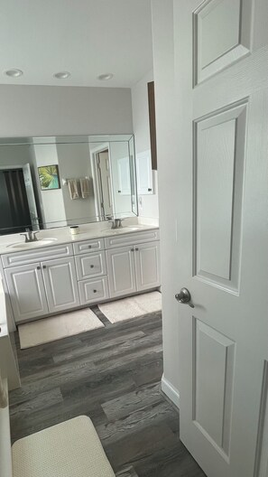 A modern bathroom with a large mirror, white cabinetry, and a wooden floor.