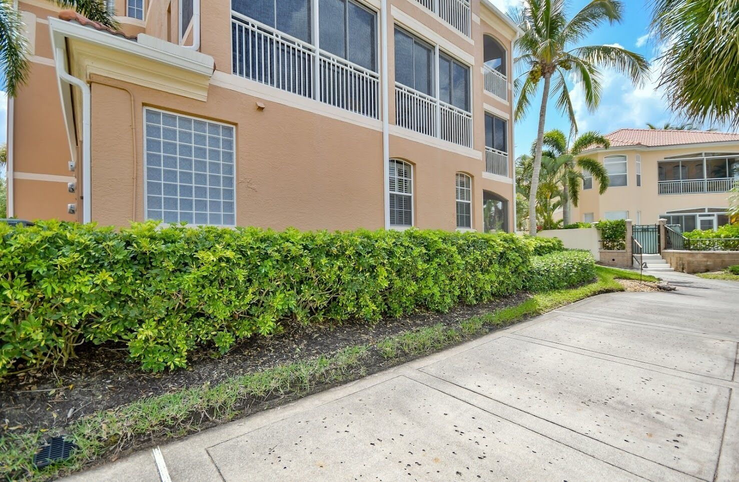 A multi-story building with balconies, a well-maintained hedge, and a clear sidewalk.