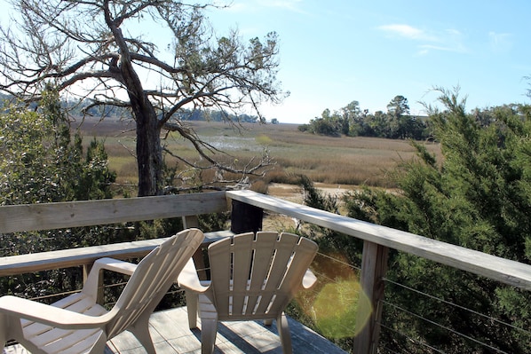 Une terrasse en bois avec deux fauteuils Adirondack donnant sur un paysage naturel, avec une rivière et des arbres.