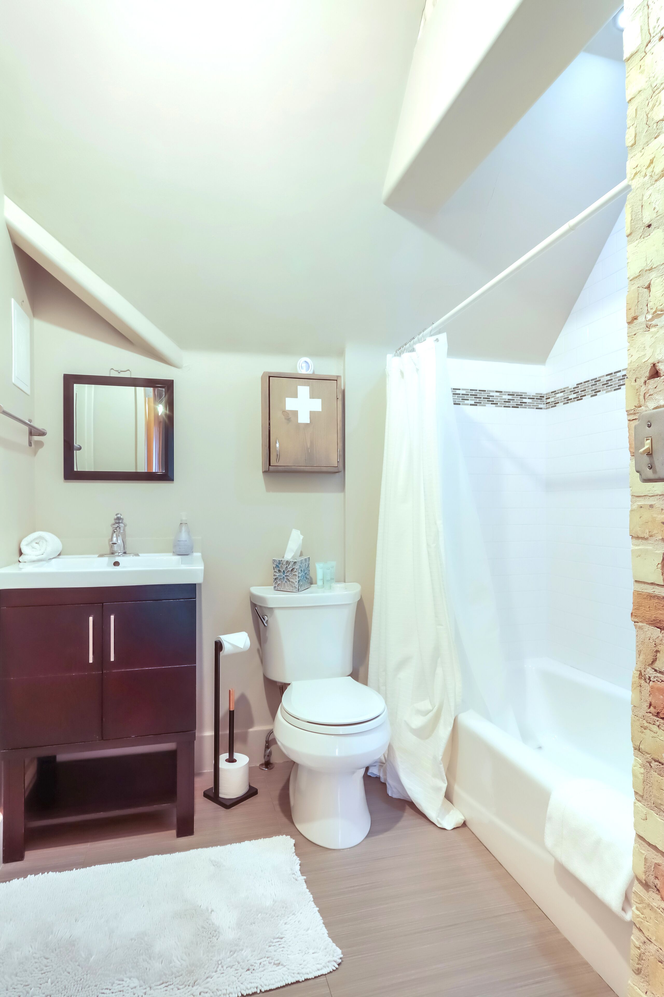 Ein Badezimmer mit einem dunklen Holzlagerflächenschrank, einer weißen Toilette und einer weißen Badewanne mit Duschvorhang.