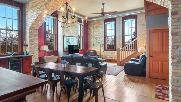 A spacious living area with a brick archway, a dining table with chairs, a sofa, a television, and a staircase.