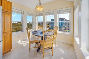 A kitchen with a round table, wooden chairs, and large windows offering a view of blue buildings and a swimming pool. - Oceanview Home w/ Private Pool, Hot Tub, Elevator, Game Room, and Home Theater (Rodanthe)