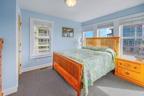 A bedroom with a wooden bed, a nightstand, a dresser, and a window with a view of a building. - Oceanview Home w/ Private Pool, Hot Tub, Elevator, Game Room, and Home Theater (Rodanthe)