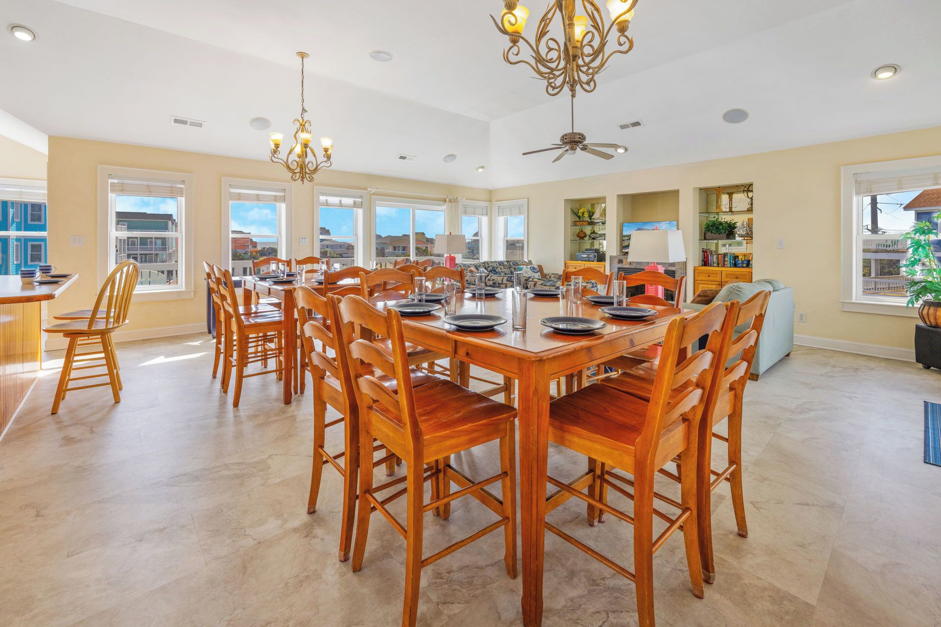 A spacious dining area with a large wooden table and chairs, a chandelier, and a ceiling fan.