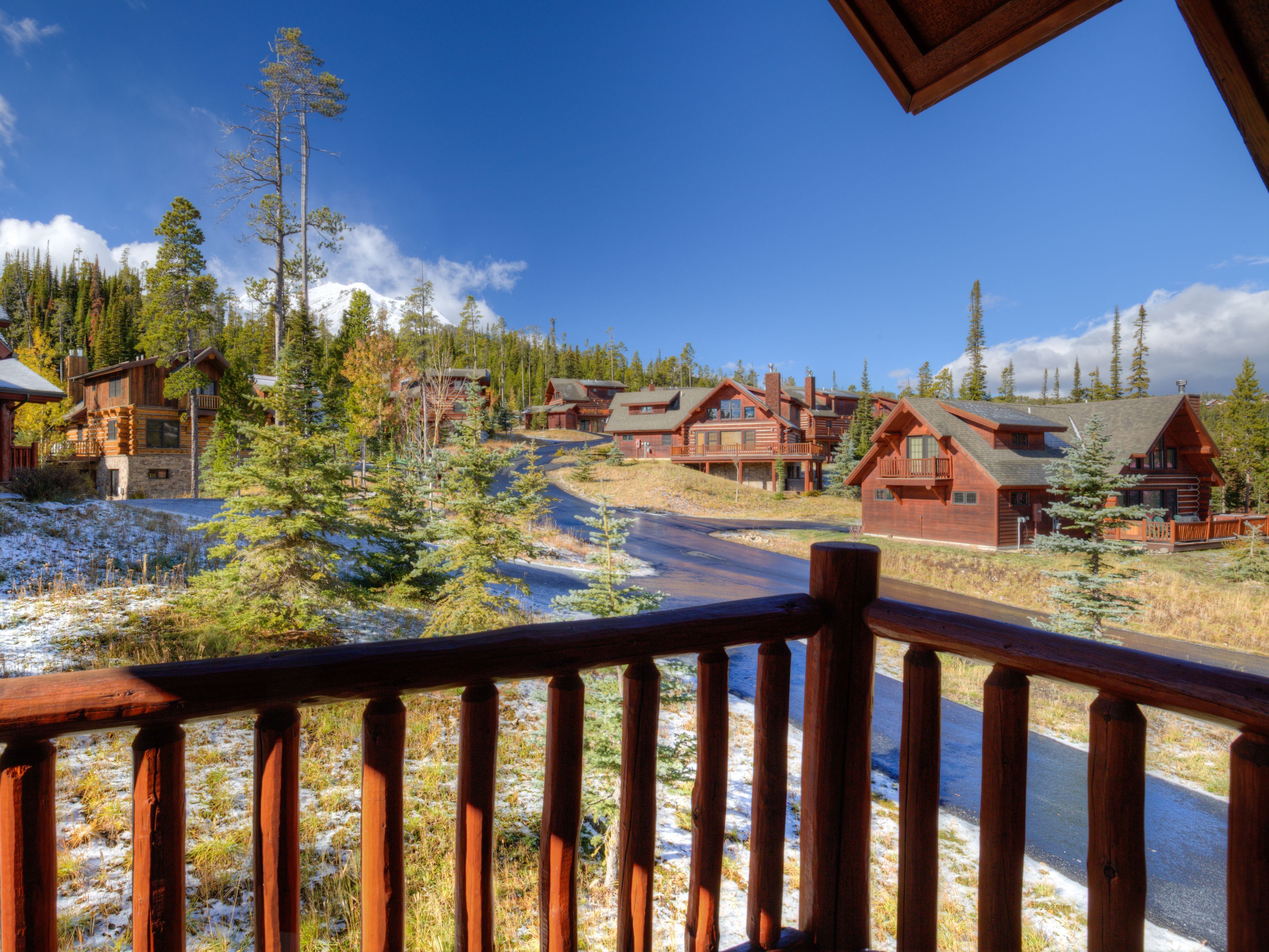 A wooden cabin with a deck overlooking a snowy landscape and a clear blue sky.