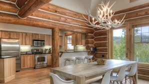 A modern kitchen with wooden beams, a large dining table, and white chairs.