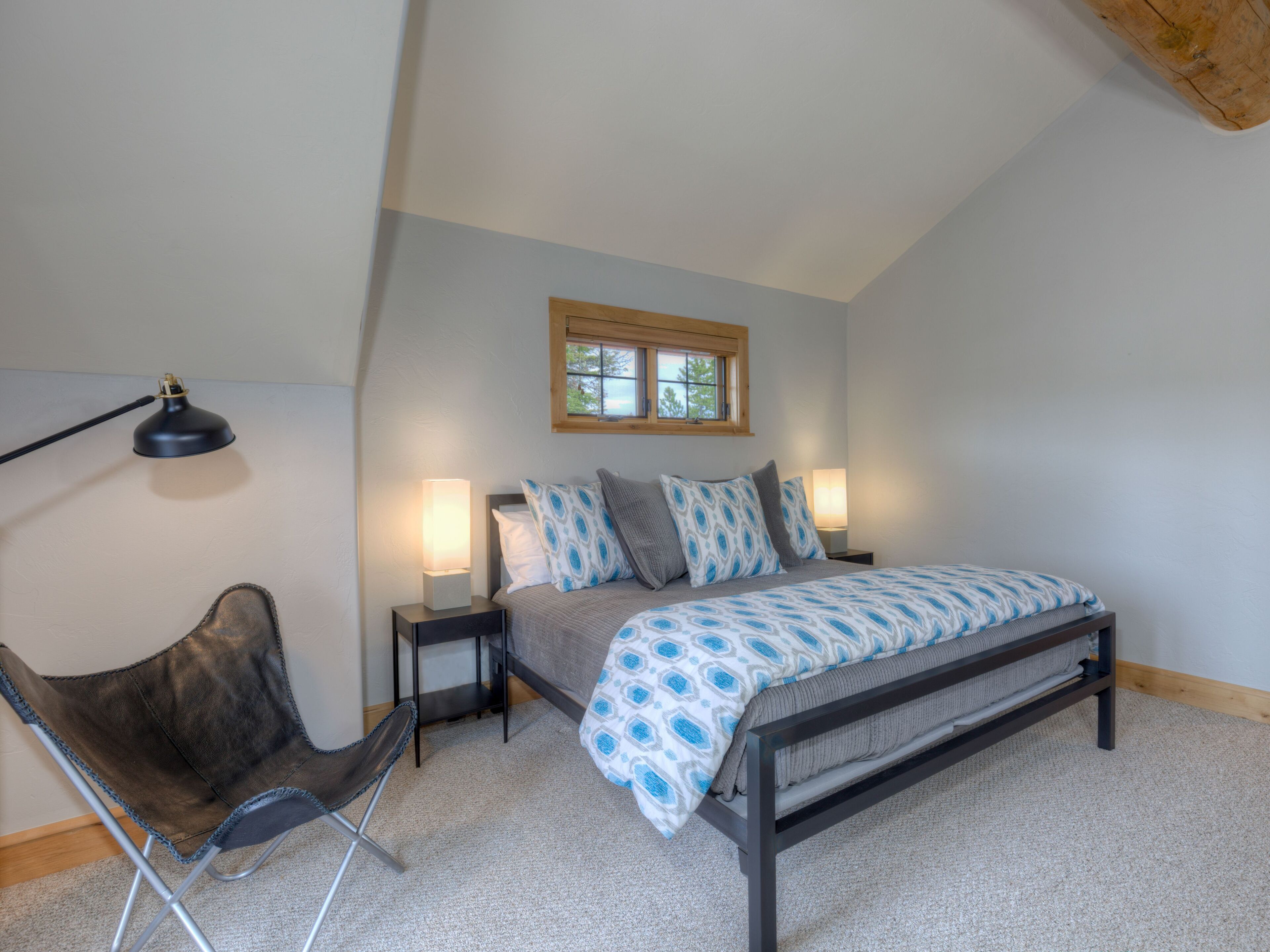 A bedroom with a bed, two bedside lamps, a chair, a window, and a ceiling light.
