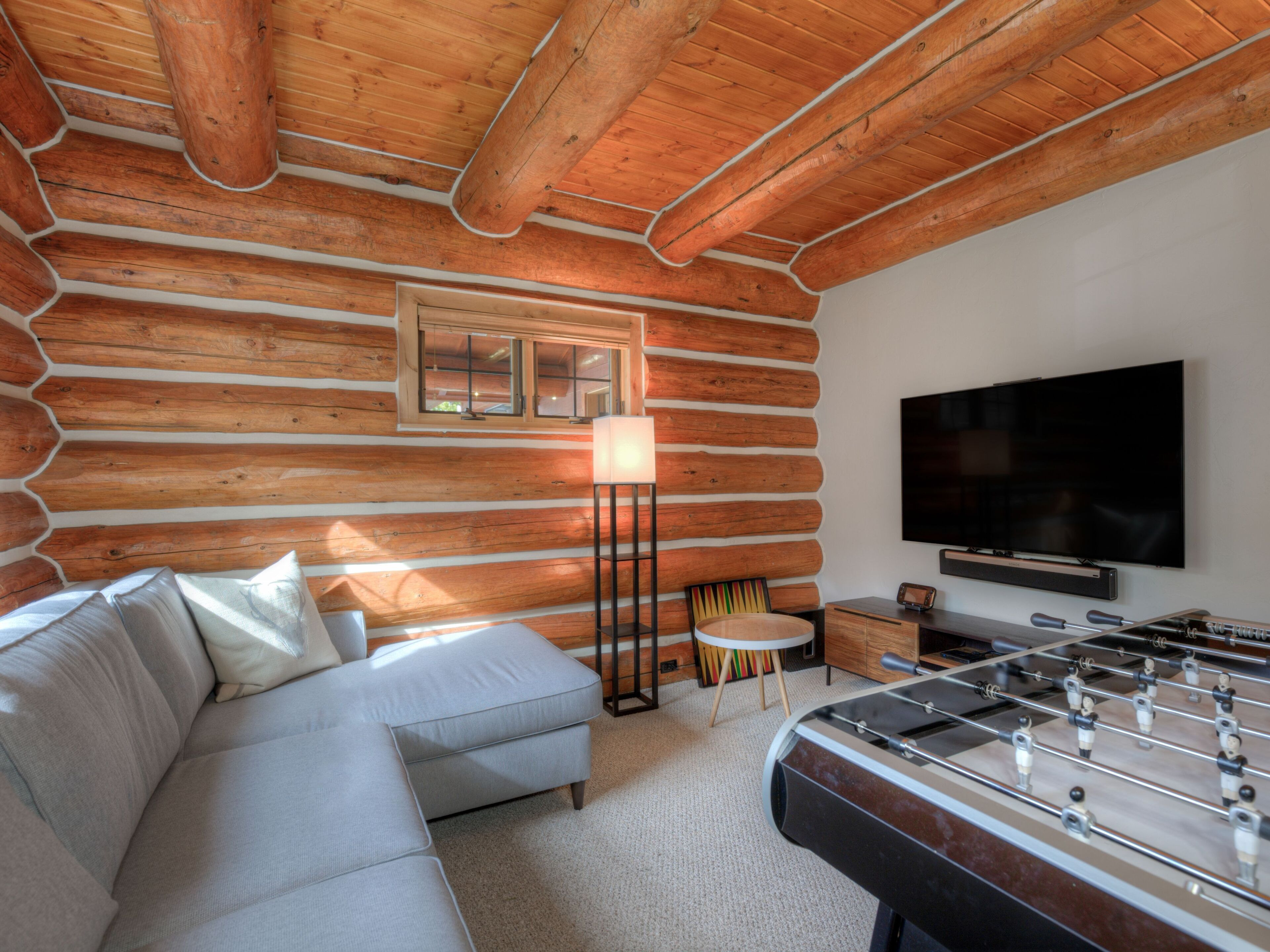 A cozy log cabin room with a sofa, a foosball table, a television, and a lamp.