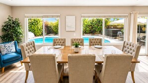 A dining area with a pool view, beige chairs, and a blue sofa. - Clear Sky Paradise - Pool, Spa & Sunset Vibes (San Diego)