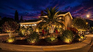 A modern house with a garage, surrounded by landscaped gardens and palm trees, under a twilight sky. - Clear Sky Paradise - Pool, Spa & Sunset Vibes (San Diego)