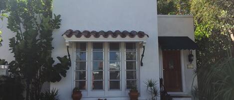 Un bâtiment blanc avec un toit en tuiles, un porche à l’avant orné de plantes en pot et une porte en bois.