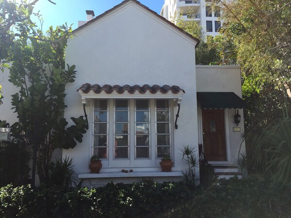 Um edifício branco com telhado ladrilhado, varanda frontal com vasos de plantas e porta de madeira.
