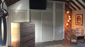 Ein Schlafzimmer mit einem hölzernen Schminktisch, weißen Klappschranktüren, einer Ziegelwand als Gestaltungselement und einer Hängeleuchte.