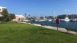 Ein Yachthafen mit vertäuten Booten, eine Rasenfläche mit Bänken und einem strahlend blauen Himmel.