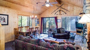 A cozy cabin interior with wooden walls, a ceiling fan, a dining area, a living room with a sofa and a TV, and a stone fireplace. - (21) River Refuge at The Redwoods In Yosemite (Yosemite National Park)