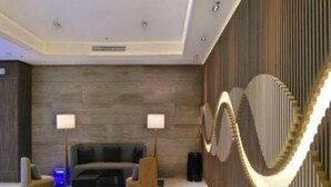 A modern hotel lobby with a dark wood wall, a curved light fixture, a sofa, and two floor lamps. - Mactan Newtown by Javadrea (Lapu-Lapu)