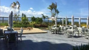 A rooftop terrace with outdoor seating, palm trees, and a view of the ocean. - Mactan Newtown by Javadrea (Lapu-Lapu)