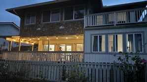 A two-story house with a stone facade, a wooden deck, and a fenced backyard. - House of the Rising Sun (Laie)