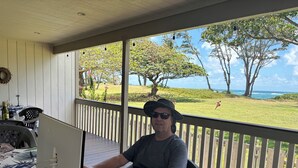A man working on a laptop on a wooden deck with a view of a grassy area and trees. - House of the Rising Sun (Laie)