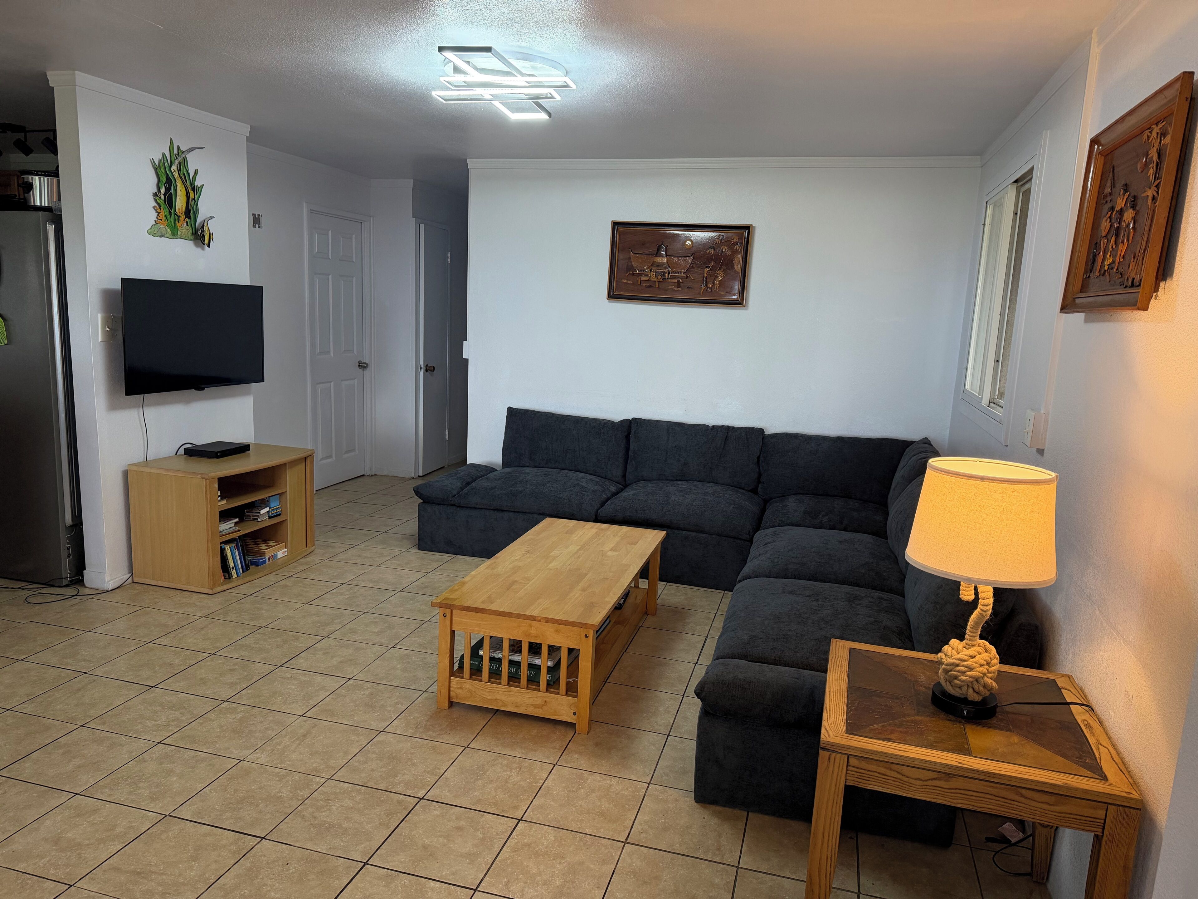 A living room with a sectional sofa, a wooden coffee table, a TV on a stand, and a lamp on a side table.