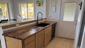 A kitchen with a wooden countertop, a black sink, and a tiled floor. - House of the Rising Sun (Laie)