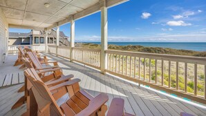 Una terraza de madera con sillas que da a una playa.
