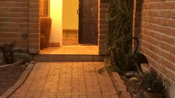 Un chemin pavé de briques mène à une porte en arc d’où émane une lumière intérieure.