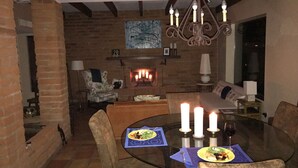 Un coin repas avec une table en verre entourée de chaises, une cheminée avec des bougies allumées et un lustre.