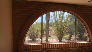 Une pièce dotée d’une grande fenêtre en arc d’où l’on peut admirer un paysage désertique parsemé de cactus et d’arbres.