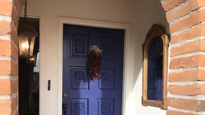 Une porte bleue ornée de motifs complexes, une plante séchée suspendue et un tapis posé sur un sol carrelé.