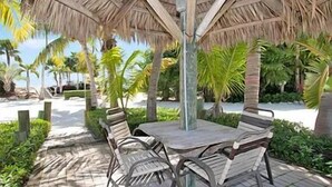 A covered outdoor seating area with a table and chairs, surrounded by palm trees and a pathway. - Coral Cove Resort - ‘A Fisherman’s Dream’ (Islamorada)