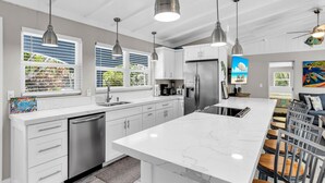 A modern kitchen with white cabinets, stainless steel appliances, pendant lighting, and a large island with bar stools. - Coral Cove Resort - ‘A Fisherman’s Dream’ (Islamorada)